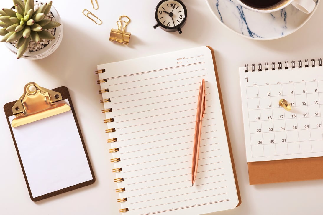 Desk with notebook, calendar, clock and plant